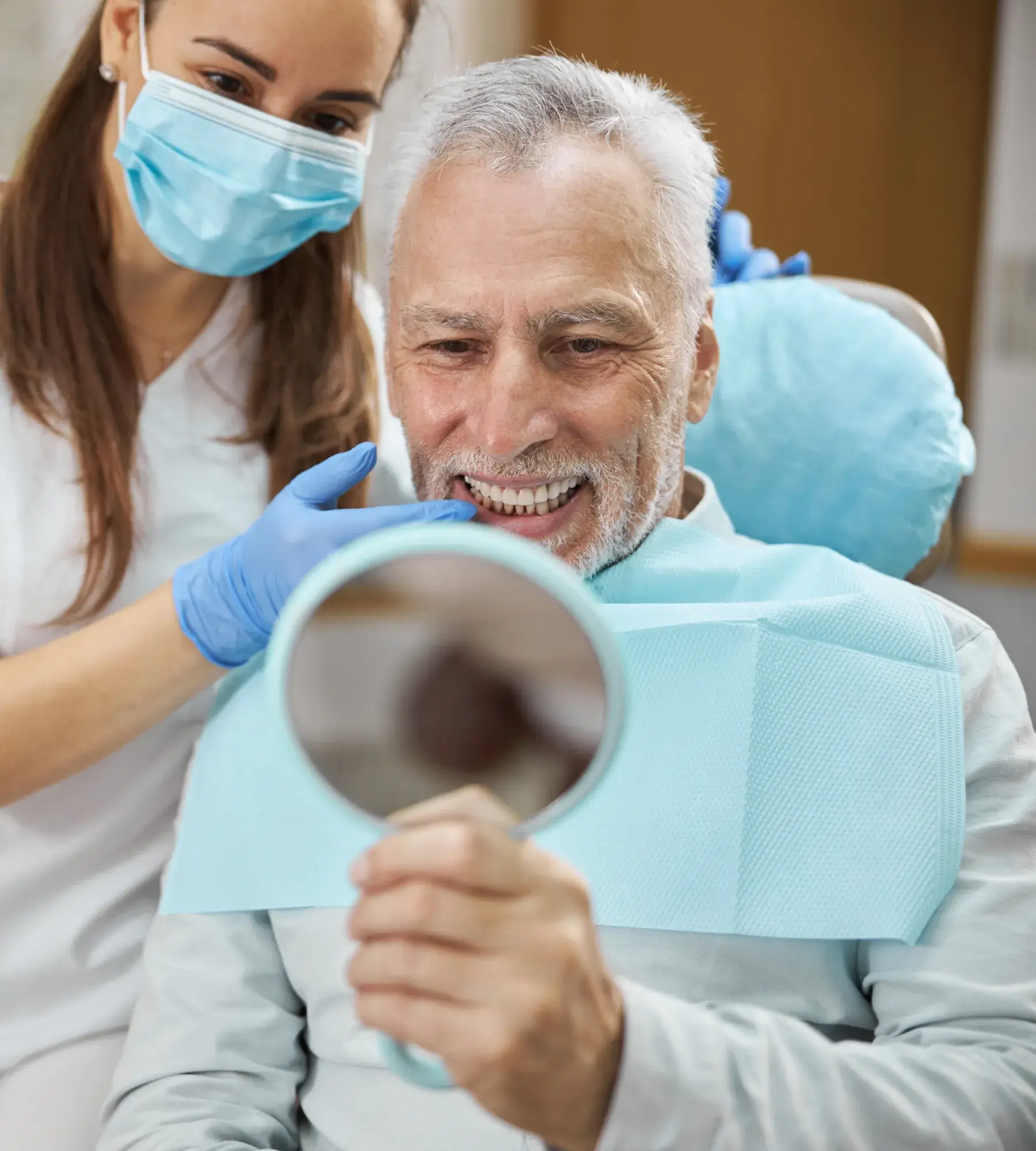 A dentist shows an older man his teeth using a handheld mirror.