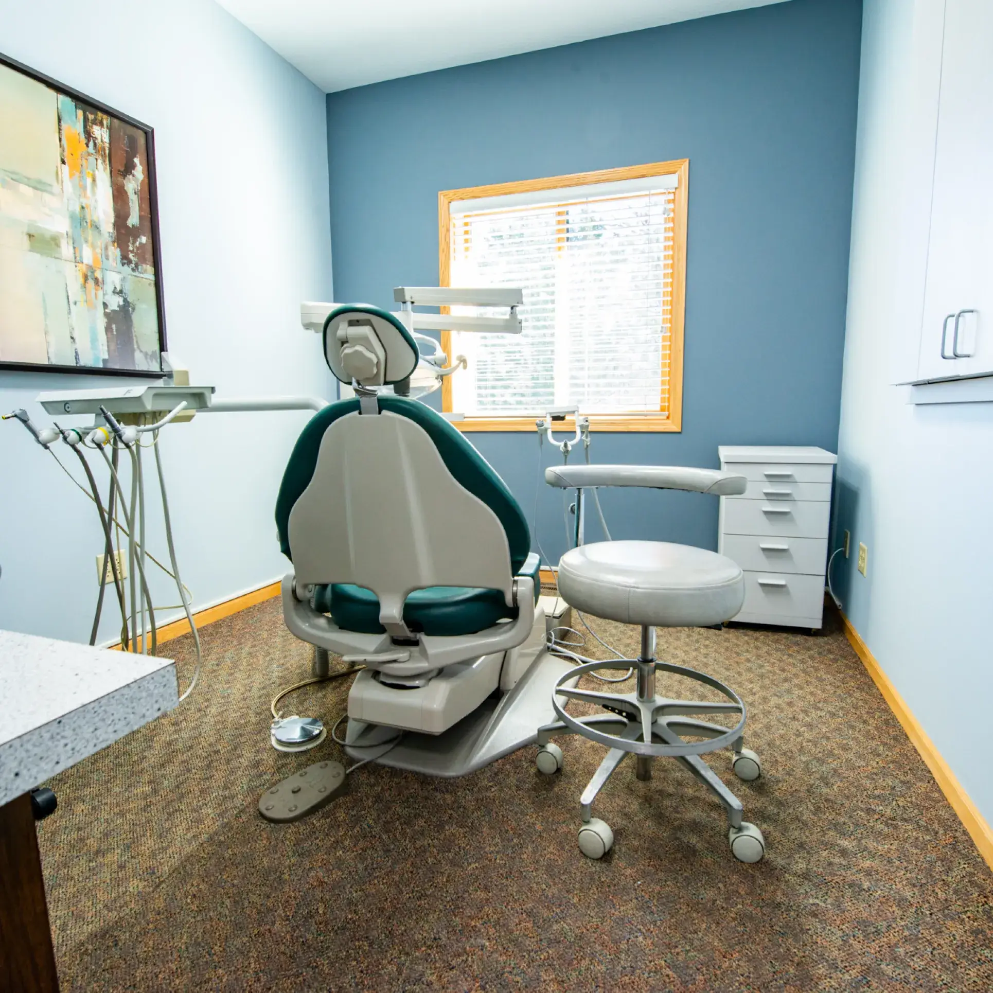 Dental examination room with a dental chair, dentist stool, and equipment on the side.