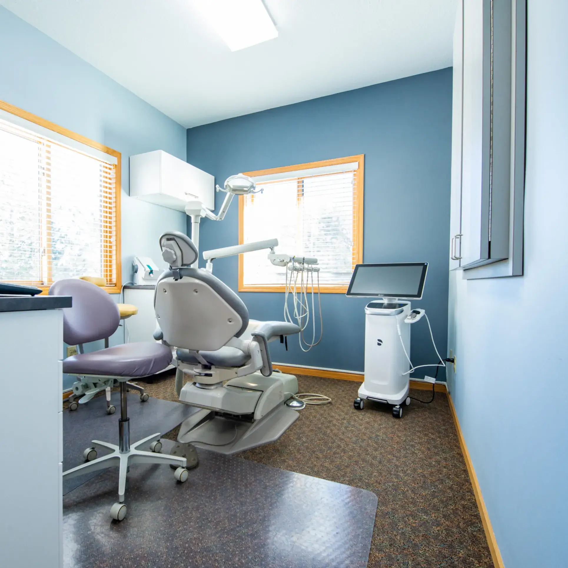 A dentist's chair and equipment in a tidy, bright dental office with blue walls.
