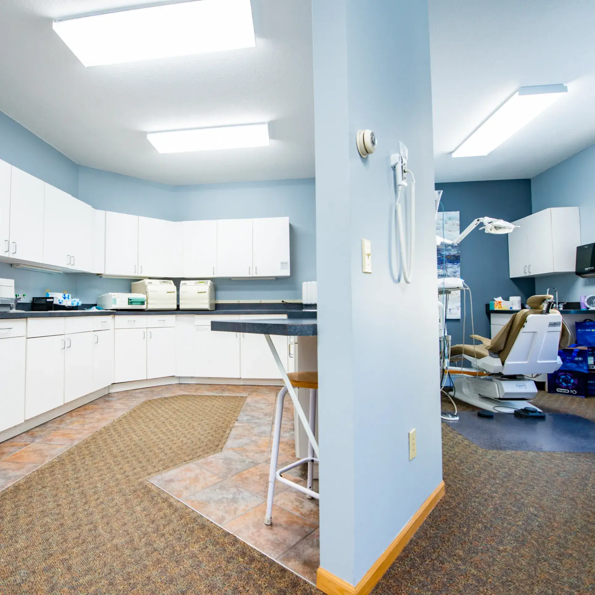 A modern dental exam room with a dentist chair, cabinets, and bright fluorescent lighting.