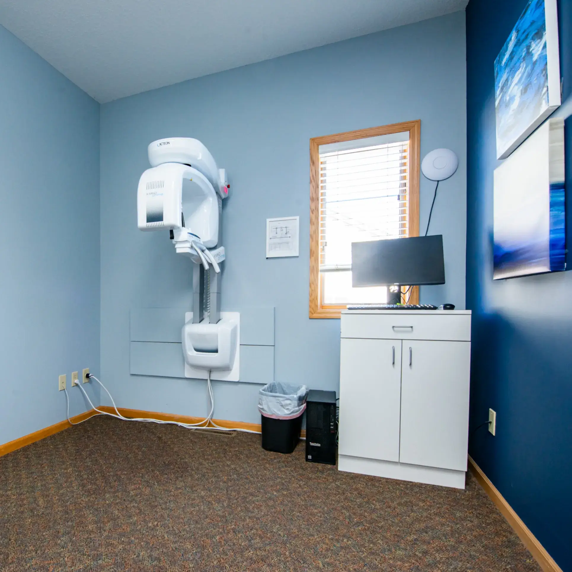 A dental X-ray machine is mounted on a wall in a small, bright room.